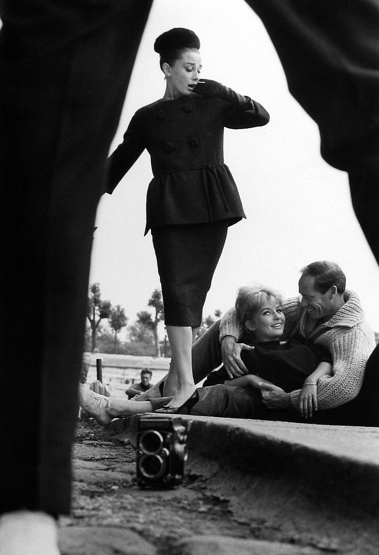 Henry Wolf - Audrey Hepburn view through legs with couple, c.1959 - Howard Greenberg Gallery