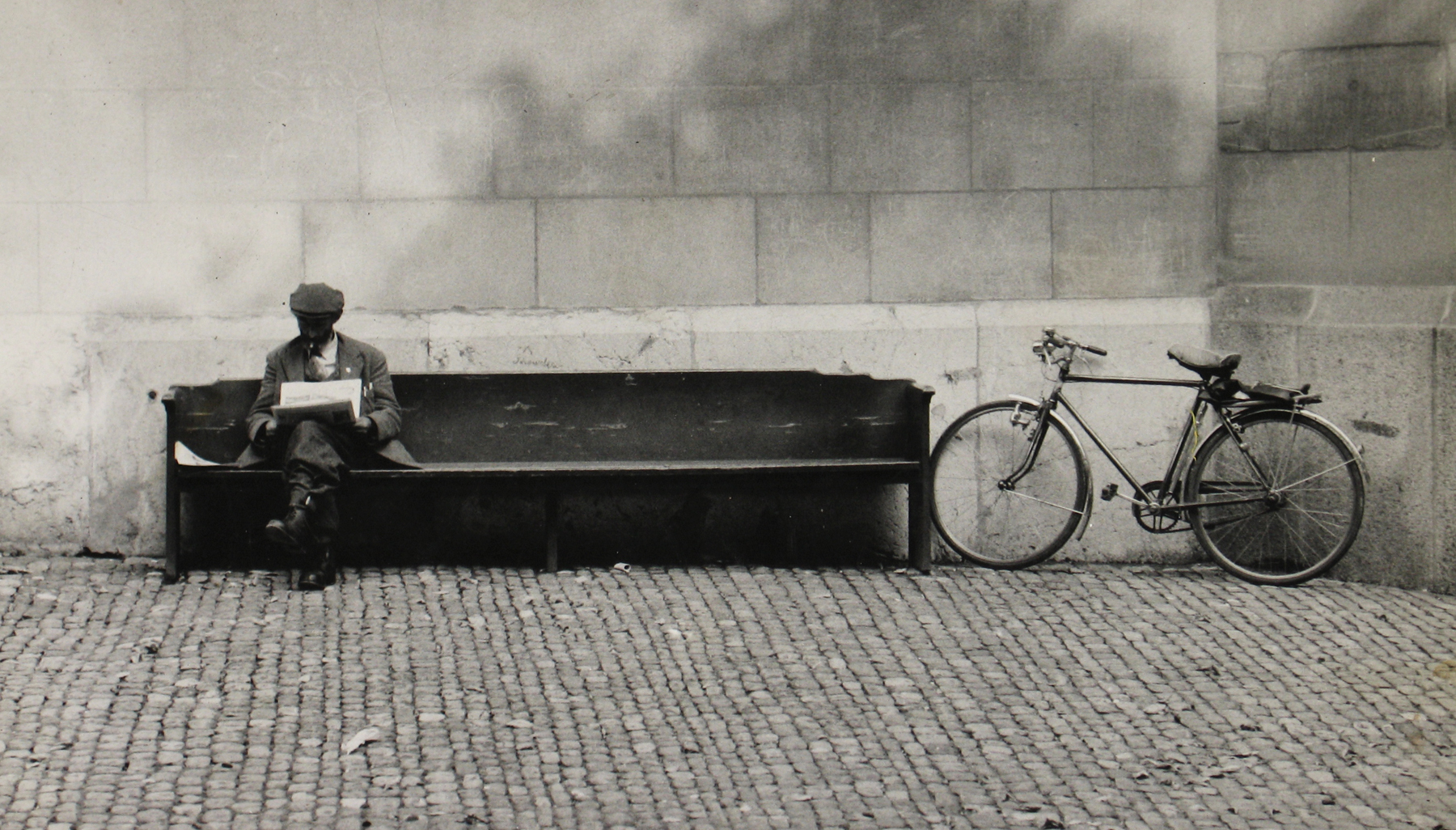 Leon Levinstein, Untitled (man on bench with parked bicycle, cobblestone), 1955, Howard Greenberg gallery, 2019